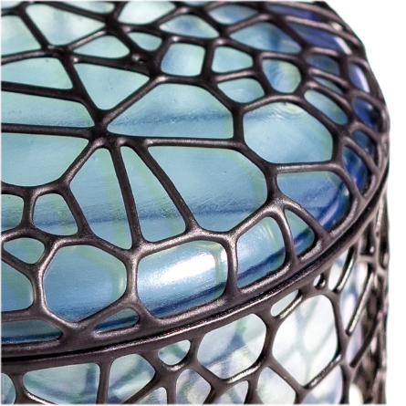 Close-up of a 3D printed jewelry box with an outer shell made of black perforated organic cellular structure and an inner chamber made of transparent bluish resin that changes color depending on the light